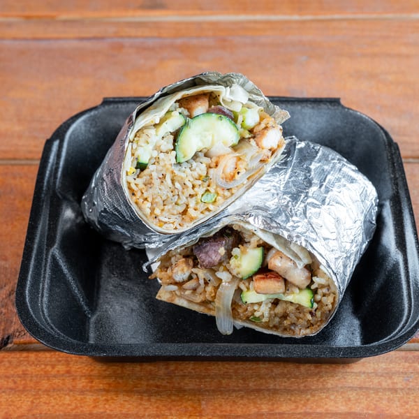 Two foil-wrapped burritos, cut in half, showing rice, zucchini, and meat, in a black takeout container.