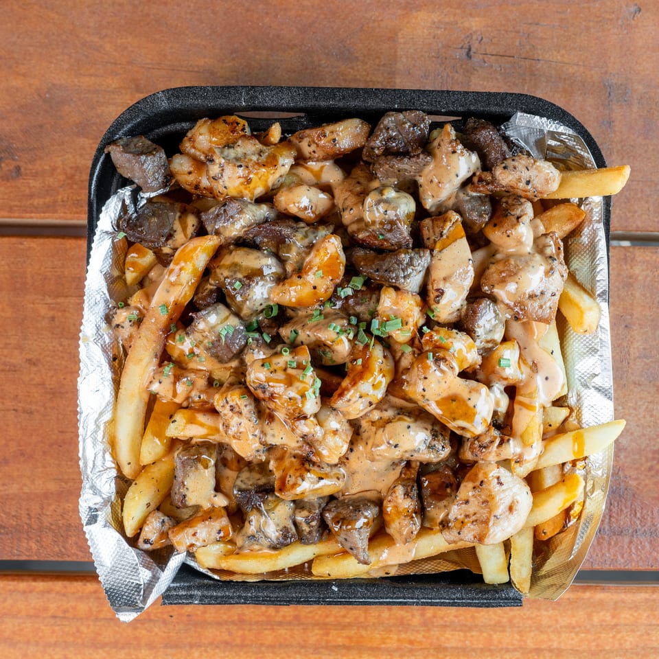 Loaded fries with chicken, steak, creamy sauce, and chives in a foil-lined container.
