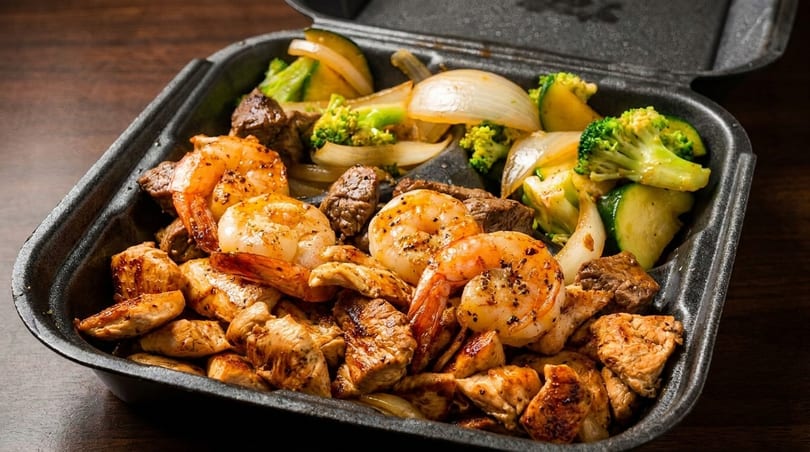 Hibachi takeout container filled with shrimp, chicken, beef, broccoli, zucchini, and onions.