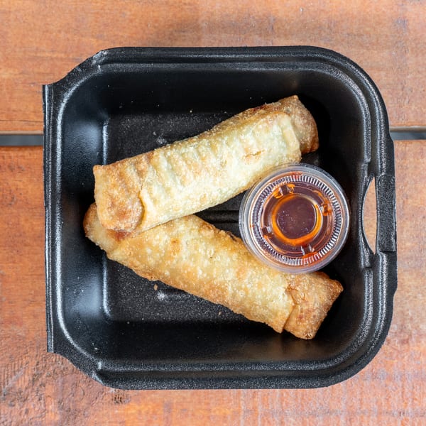 Golden egg rolls with dipping sauce in a black to-go container on wood.