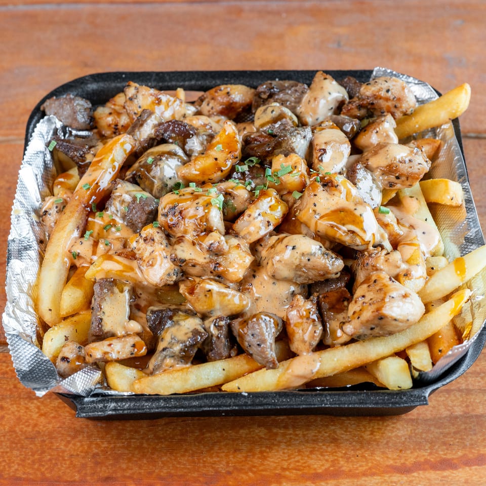 Golden french fries, chicken, and beef pieces covered in creamy sauce and chives in a black container.